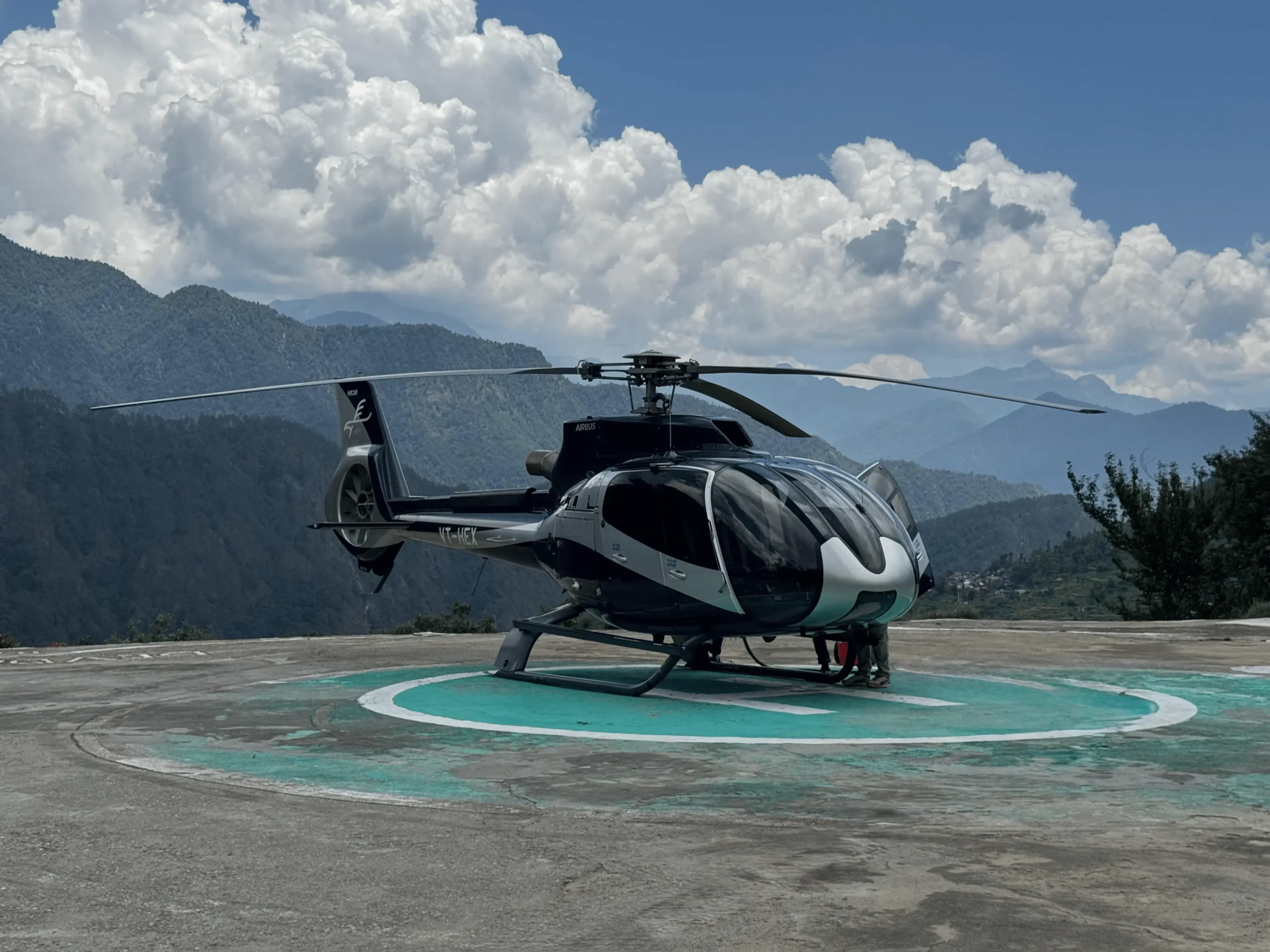 Luxury helicopter parked on a helipad for Do Dham Yatra by helicopter with Avya Aviation and Himalayan hills in the background.