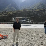 A traveler standing on a mountain helipad with a premium passenger helicopter and massive Himalayan peaks behind him During the Chardham Helicopter booking.