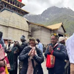 An elderly couple with folded hands praying in front of the historic Kedarnath Temple during their Chardham yatra by helicopter.