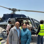 An elderly couple smiling happily next to an Airbus passenger helicopter on the helipad during their Chardham yatra package by helicopter.