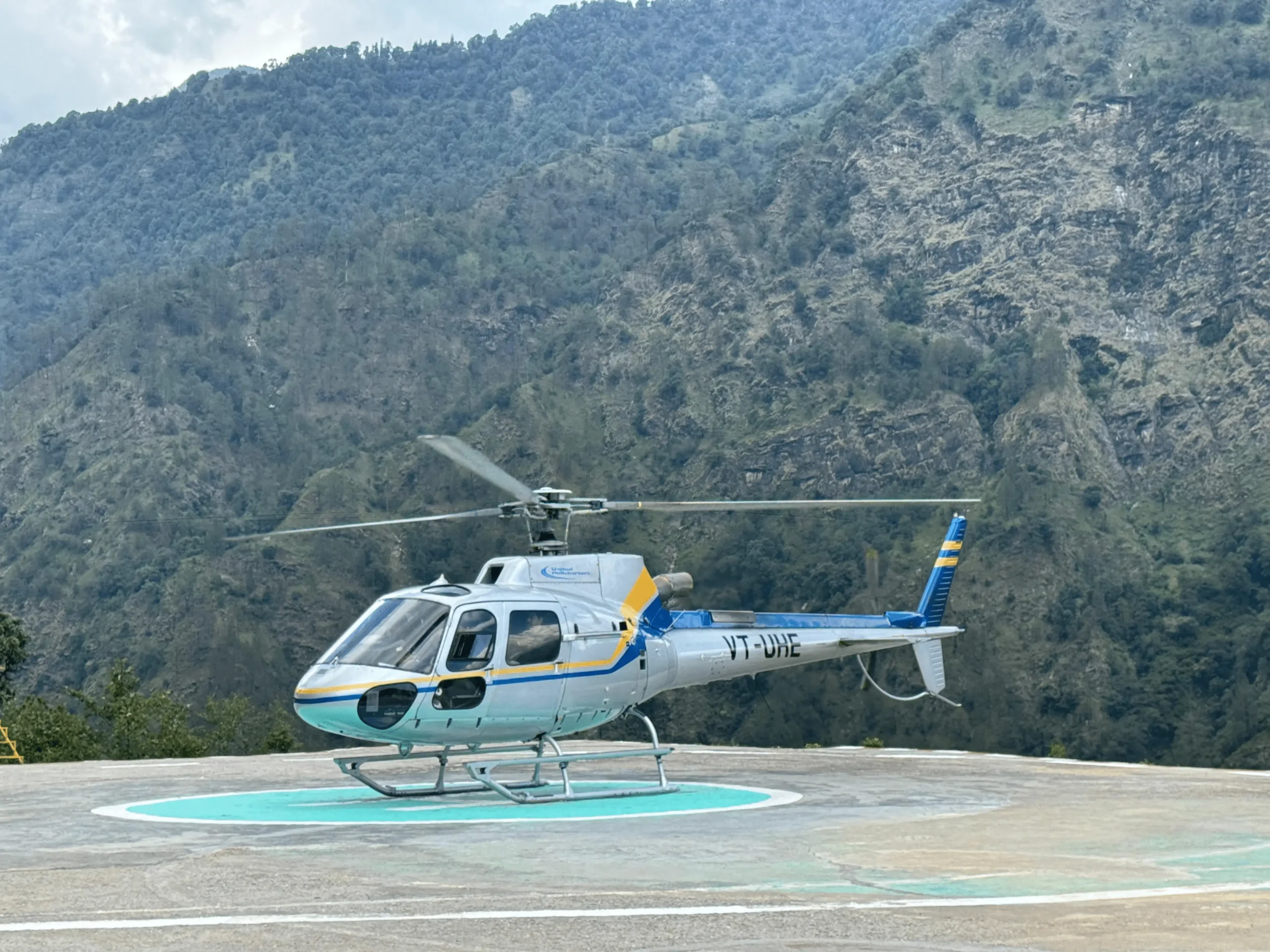 White and blue shuttle helicopter parked on kedarnath helipad for 2 Dham Yatra package by helicopter.
