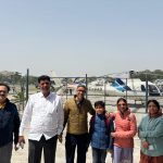A happy family standing at the helipad during their 4 Dham yatra by helicopter tour, with a white and blue color helicopter in the background.